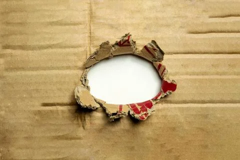 A ragged, circular hole torn through a brown corrugated cardboard sheet, re.. Stock Photos