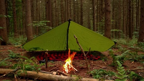 Raging campfire in front of Bushcraft style tarp setup. Video stock 86571416