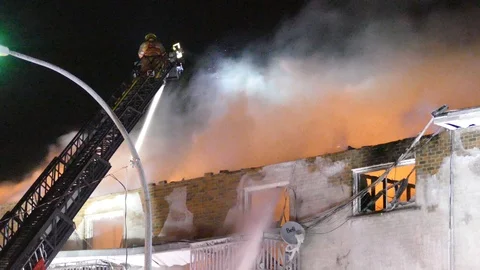 Raging fire in windy conditions with fireman atop ladder set up over it Vídeos de archivo 103452214