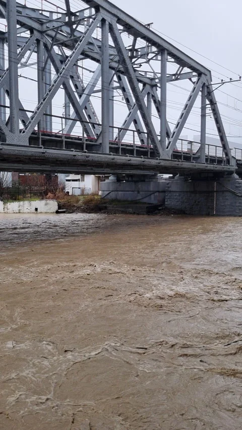 Raging muddy river flowing rapidly beneath a steel truss railway bridge after Stock Footage 328505256