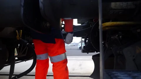 Rail Worker in Hi-Vis Inspecting Train Undercarriage in Overcast Freight Yard Stock Footage 338371608