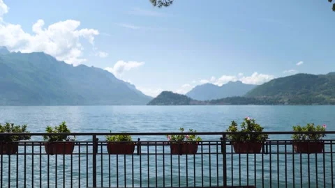 Railing with flower pots and bench with blurry mountains of lake como italy Stock Footage 276681353