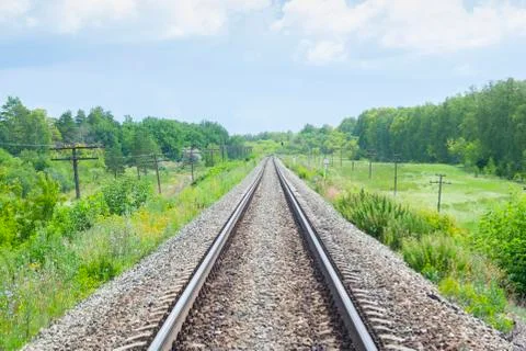 A railway through the summer green fields.  Beautiful green railway tree land Stock Photos