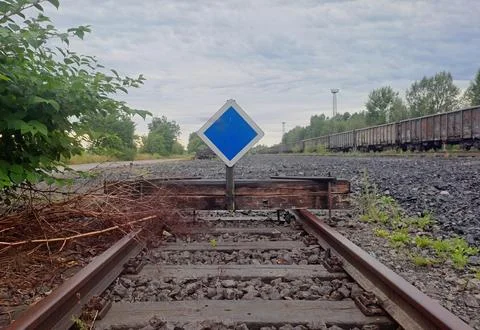 Railway track ending at a buffer stop with blue railway sign. Stock Photos