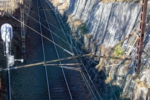 A railway track with overhead electrification systems and a rocky reinforced Stock Photos