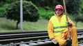 Railway worker in yellow uniform with shovel in hand sits on railway line HD Footage