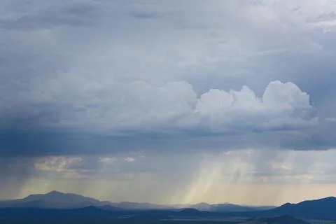 Rain and dark storm clouds fill the sky. Mountains are in the background. Stock Photos