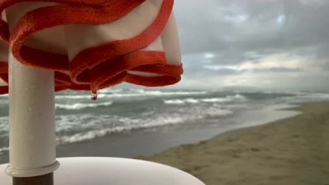 Rain on the beach. Raindrops drip from a wet folded parasol against a Stock Footage 164526268