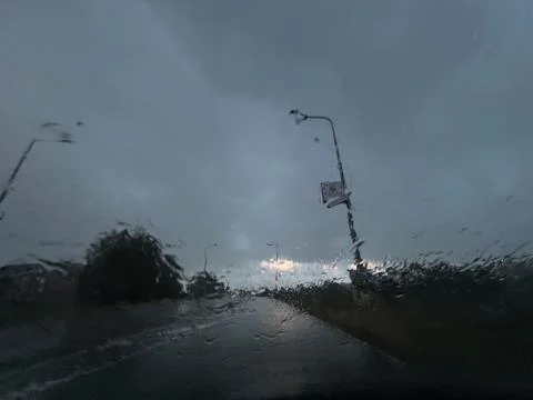 Rain blurred road under dark storm clouds with streetlights and wet Stock Photos