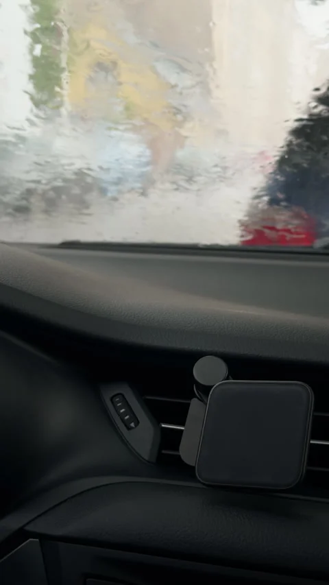 Rain blurred windshield from car interior with dashboard air vent and phone Stock Footage 345605414