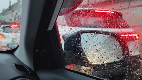 Rain on car window with traffic brake lights and side mirror view Stock Footage 344850831