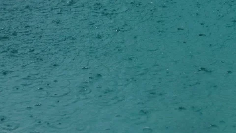 Rain cascading onto turquoise water surface creates ripples, circles, and Stock Footage 312743458