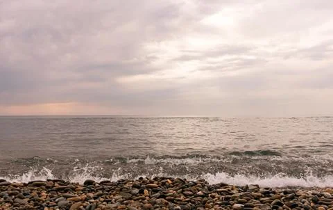 Rain clouds over the sea at sunset. Pebbles on the beach close-up, clouds Stock Photos