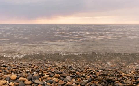 Rain clouds over the sea at sunset. Pebbles on the beach close-up, clouds Stock Photos