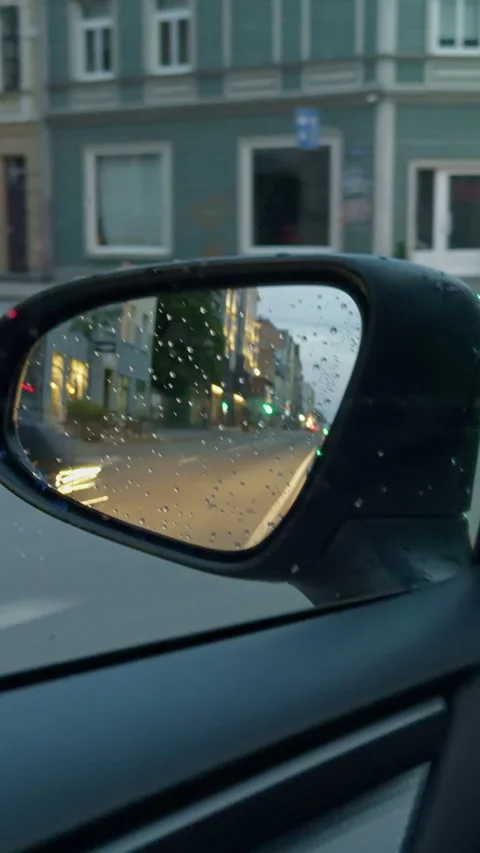 Rain covered car side mirror reflecting blurred city street, glowing traffic Stock Footage 345124825