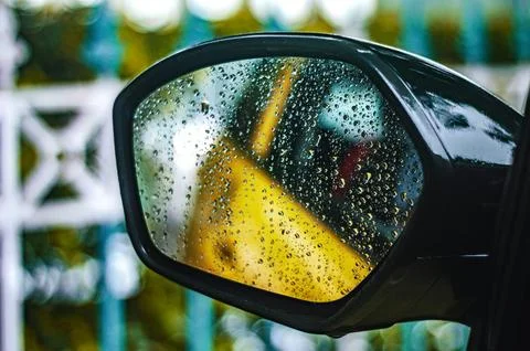 Rain-covered vehicle side mirror sharply captures water droplets and a yell.. Stock Photos