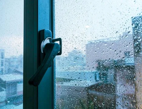 Rain-covered window handle with blurry outdoor view Stock Photos
