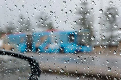 Rain droplets on a car side window, looking out. Defocused blue bus Stock Photos