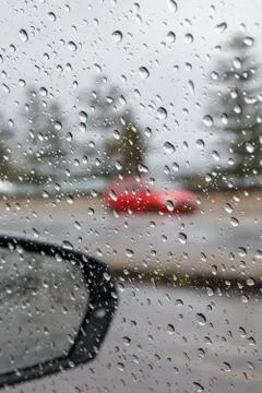 Rain droplets on a car side window, looking out to defocused street w/red car Stock Photos