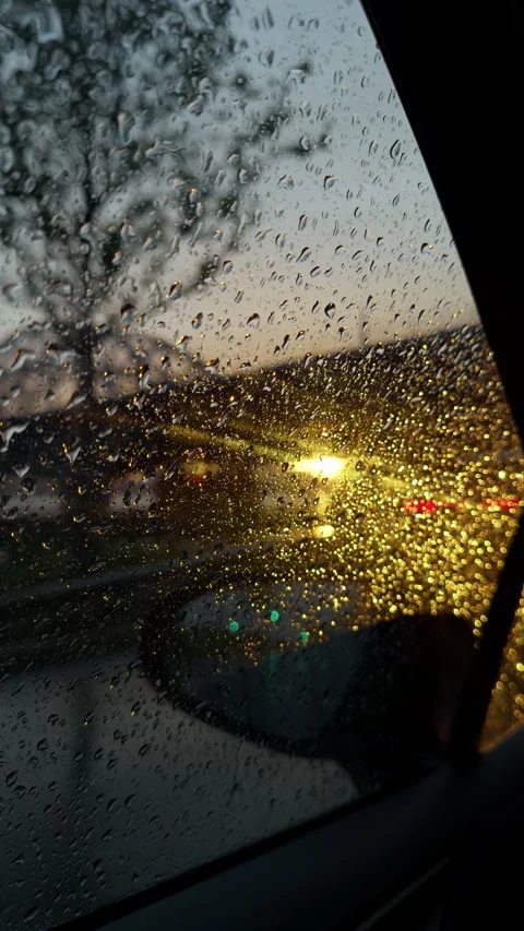 Rain droplets on car window with blurred traffic lights and dusk glow during wet Stock Footage 345766674
