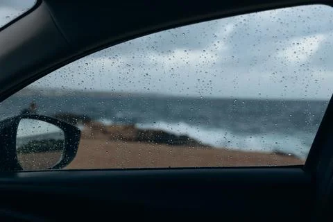 Rain droplets on car window create a blurred view of the ocean waves crashi.. Foto stock
