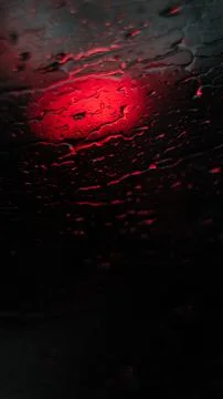 Rain droplets on a dark surface reflect vivid red light, creating a strikin.. Stock Photos