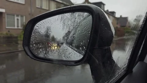 Rain drops on a car side mirror on a gloomy wet day with cyclist in background Stock Footage 344161797