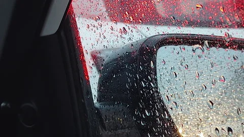 Rain drops on car side mirror with red taillight reflection close up Stock Footage 344850562