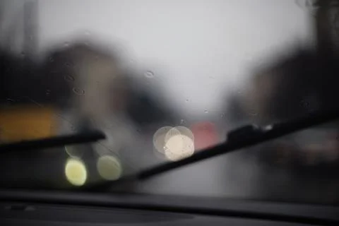 Rain drops on a car windshield with blurred street lights and wipers in motio Stock Photos