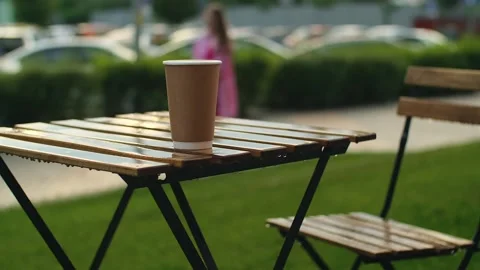 Rain drops dripping on paper coffee cup. Wooden tables of open terrace under Stock Footage 251732513