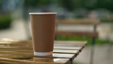 Rain drops dripping on paper coffee cup. Wooden tables of open terrace under Stock Footage 251738191