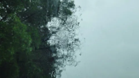 Rain drops falling on car window with blurred green forest background Stock Footage 344850249