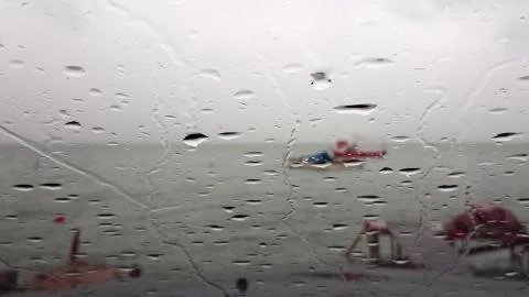 Rain drops falling on car window against sea waves on a rainy day. Stock Photos