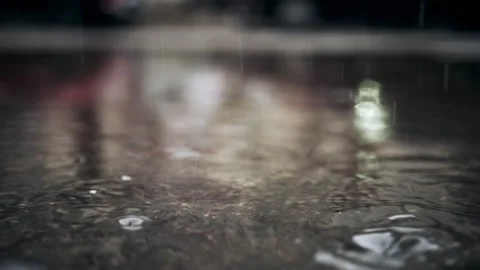 Rain drops falling into dark puddle on asphalt creating ripples and bubbles.. Stock Footage 339644658