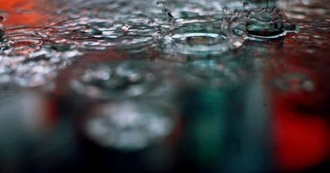 Rain drops falling into puddle. Urban lights reflection on water surface Stock Footage 127317199