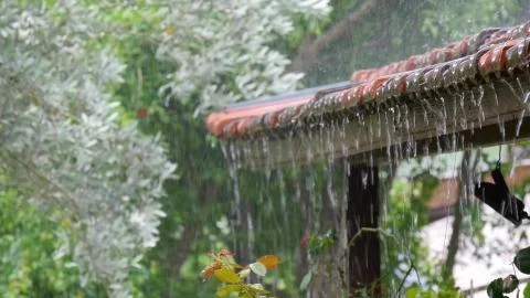 Rain drops falling from roof's eave during rain. Stock Photos