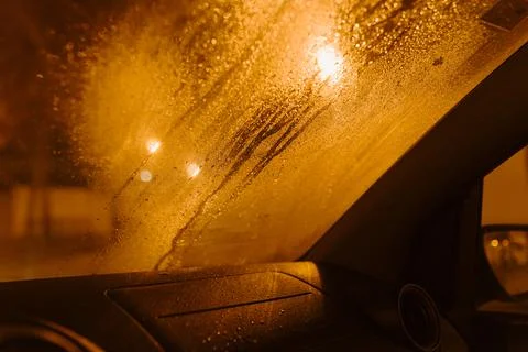 Rain drops in a raining day on window car with lamp street. Dewdrops. Stock Photos