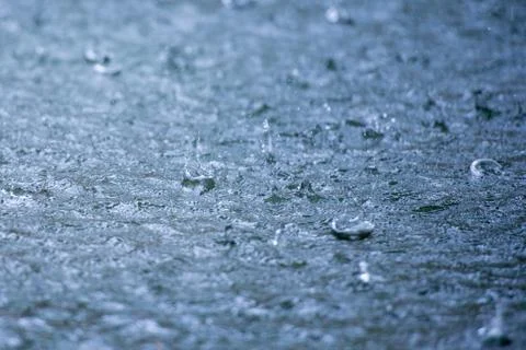 Rain drops rippling in a puddle with blue sky reflection Stock Photos