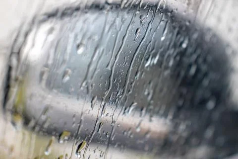 Rain drops rolling on window in storm, and a blurred black car side view mirr Stock Photos