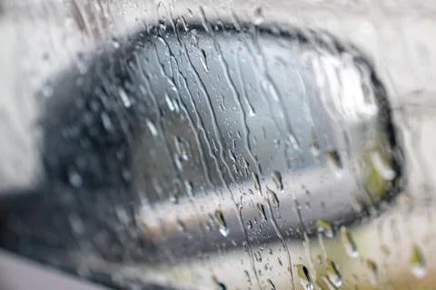 Rain drops rolling on window in storm, and a blurred black car side view mirr Stock Photos
