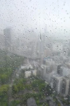 Rain drops running down a window, with a city scape just visible. Stock Photos