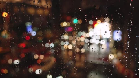 Rain drops on window with blurred city traffic lights at night creating Vidéo 318462291