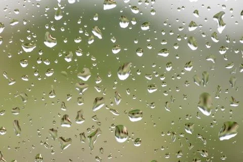 Rain drops on window with building and green tree in background Stock Photos