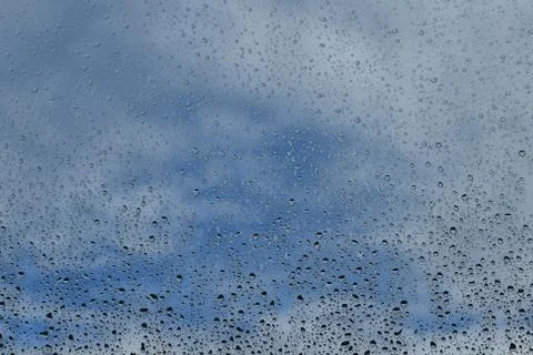 Rain drops on window with cloudy blue sky background Stock Photos