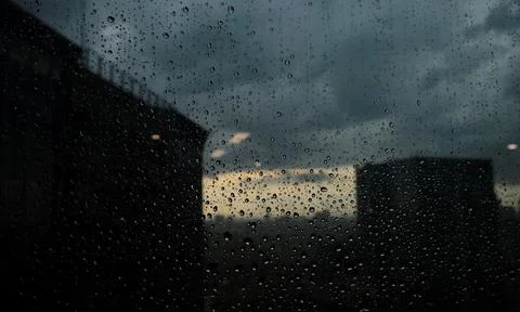 Rain drops on window with dark city and sunset view. Stock Photos
