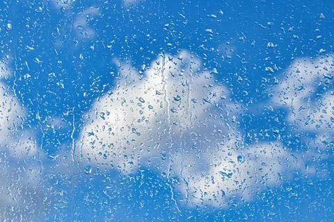 Rain drops on window glasses surface with blue sky and clouds background. R.. Stock Photos