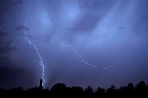 Rain falling and stroke of forked lightning during thunderstorm at night over Fotos Stock