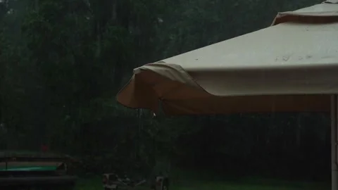Rain falling from a beige patio umbrella in a garden Vidéo 314897809