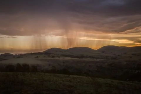 Rain falling on a distant mountain with orange sunset Stock Photos