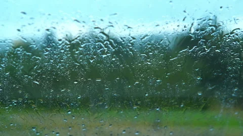 Rain falling on glass window with blurred green trees in background Stock Footage 321594385
